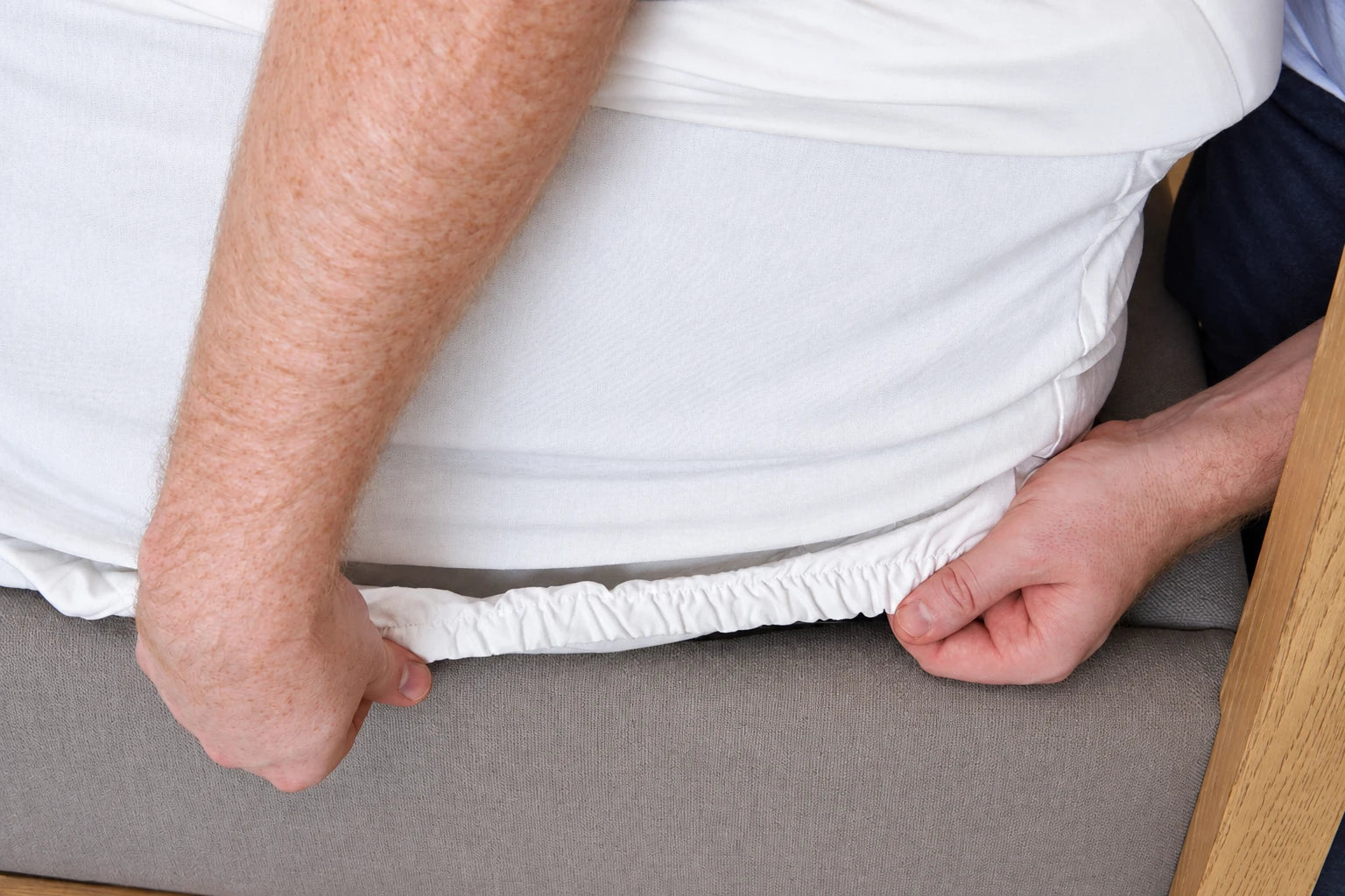 Hands fitting the elastic edge of the topper case around the mattress